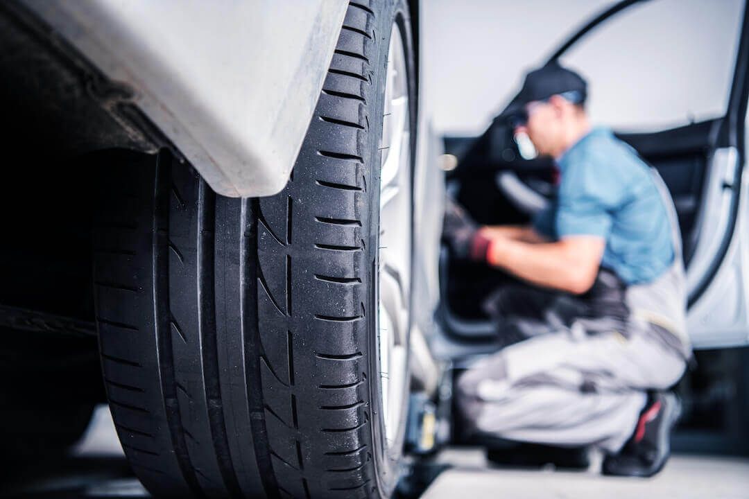 Back tire with blurry view of mechanic performing scheduled warranty car service