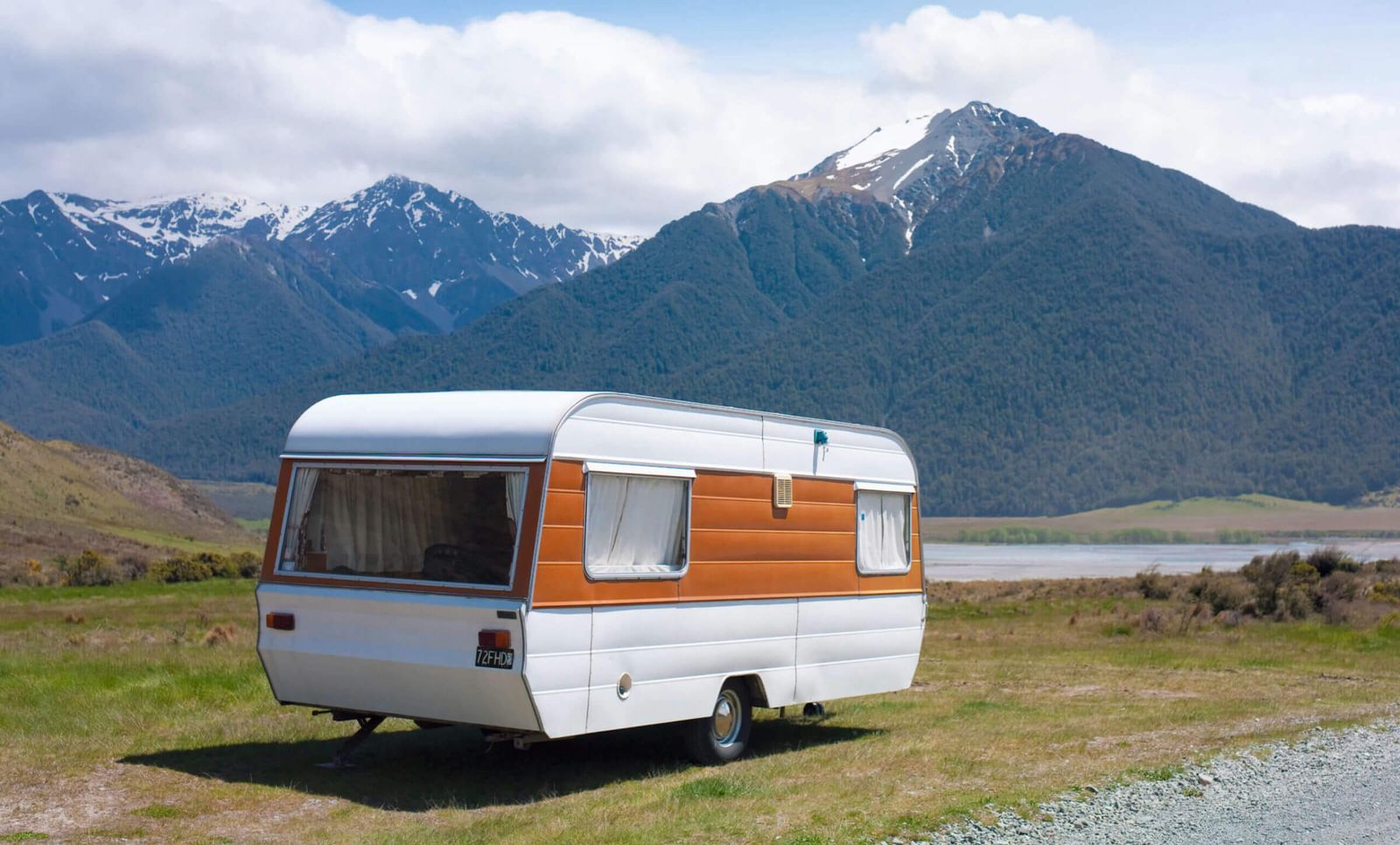 An old orange and white colored caravan located in a rocky mountain landscape