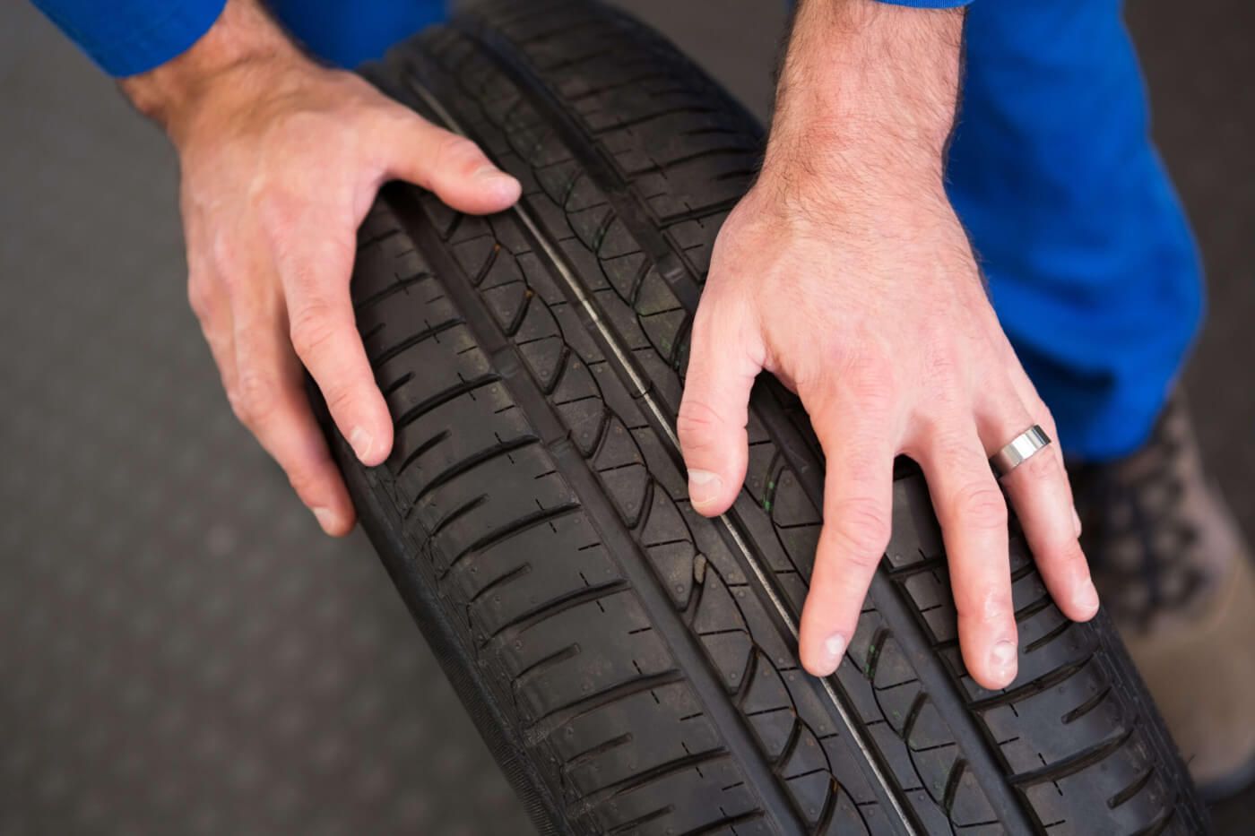 Close-up of a mechanic rolling the tire on the ground to check the depth of its tread