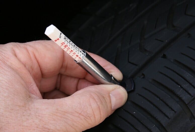 Close up view of a hand measuring the tire tread depth using a gauge